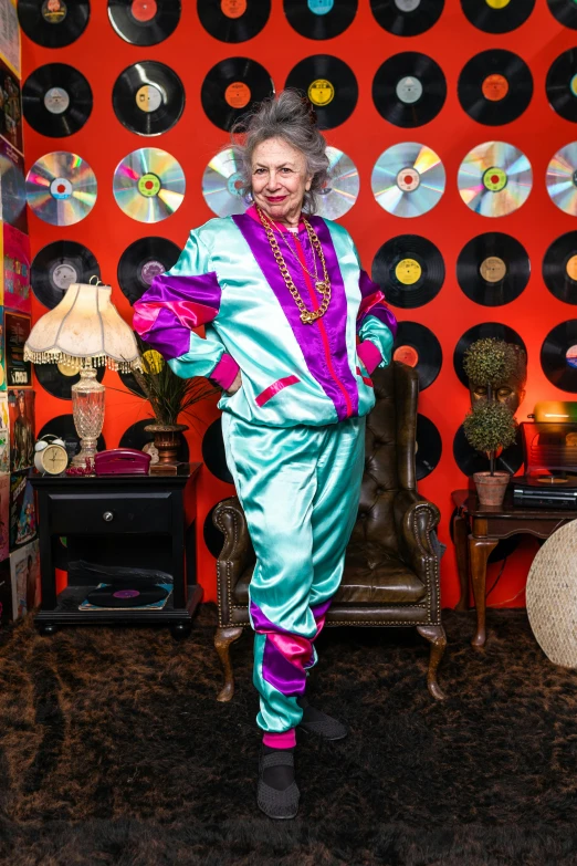 a woman standing in a room with a record wall behind her, inspired by Norma Bull, maximalism, wearing a track suit, an elderly, platinum attire, brightly colored