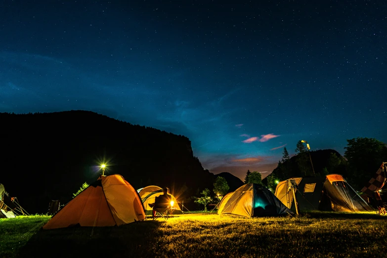 a group of tents sitting on top of a lush green field, pexels contest winner, night light, thumbnail, blue and orange rim lights, conde nast traveler photo