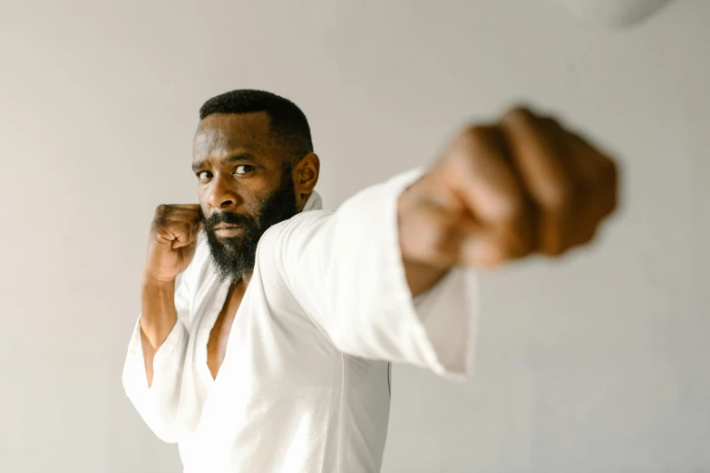 a close up of a person with a fist, pexels contest winner, figuration libre, wearing a white gi, man is with black skin, looking confident, upper body image