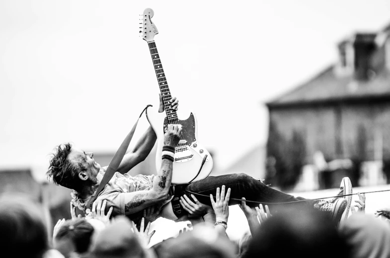 a black and white photo of a man playing a guitar, by Gavin Nolan, pexels contest winner, happening, liberty leading the people, punk rock with mohawks, laying on roses, music festival