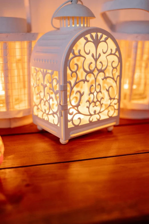 a couple of white lanterns sitting on top of a wooden table, warm lighting inside, detailed filigree, detail shot, soft light - n 9