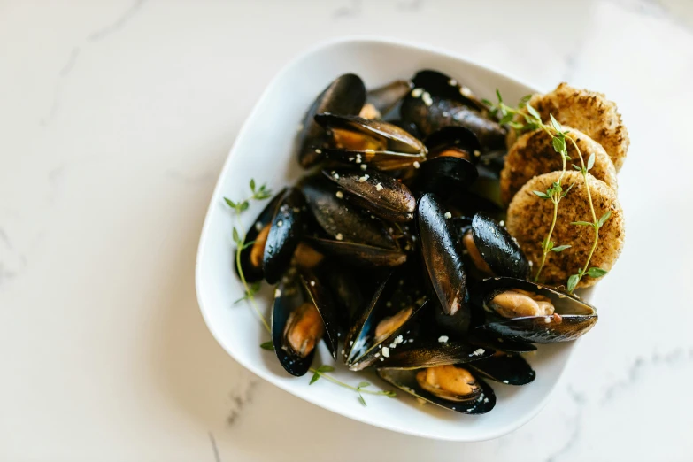 a bowl of mussels and bread on a table, pexels contest winner, fan favorite, ivy's, black and blue scheme, liquid gold