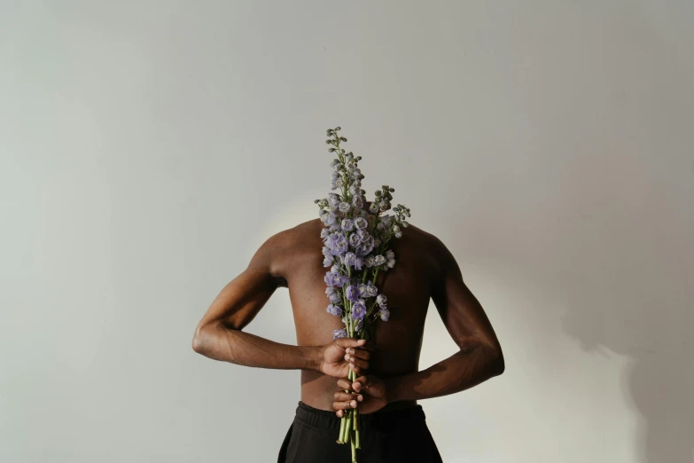 a man holding a bunch of purple flowers, inspired by Robert Mapplethorpe, trending on pexels, brown skinned, graceful body structure, monia merlo, videogame still