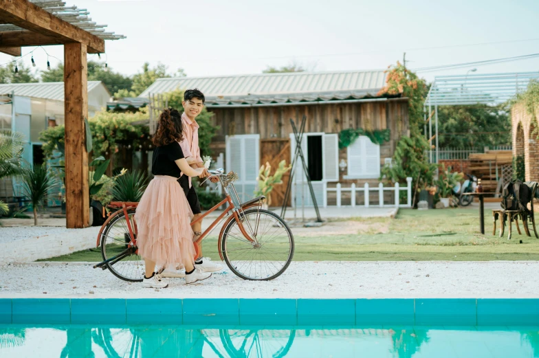 a man and a woman standing next to a swimming pool, pexels contest winner, happening, riding a bike, romantic themed, nivanh chanthara, a wide full shot