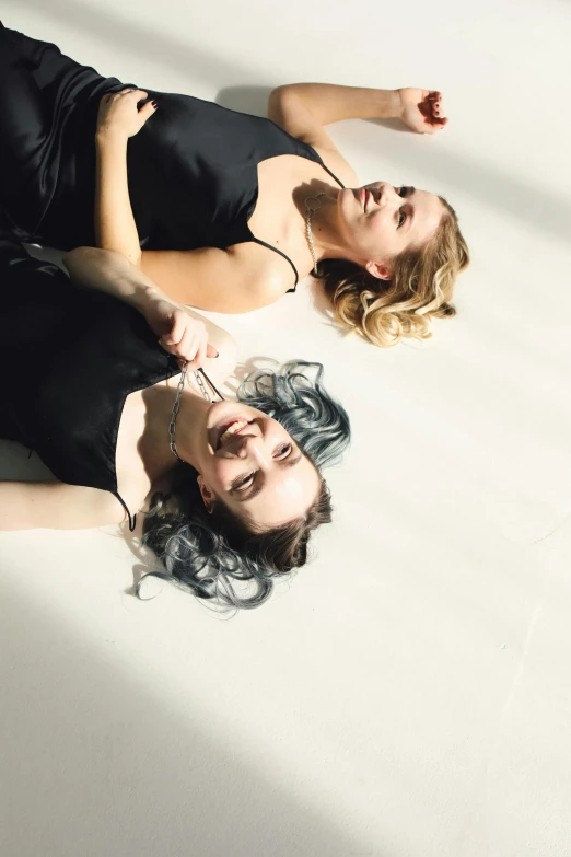 a couple of women laying on top of a white floor, by Sara Saftleven, trending on pexels, bauhaus, hair, silver light, silk, concert