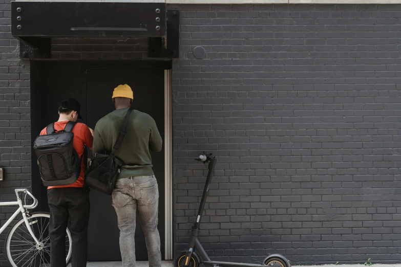 two men standing outside of a building next to a scooter, pexels contest winner, private press, lush brooklyn urban landscaping, about to enter doorframe, on a black wall, a group of people