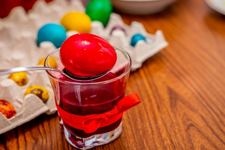 a glass filled with red liquid sitting on top of a wooden table, inspired by Ernő Grünbaum, holding easter eggs, multi colour, square, greek