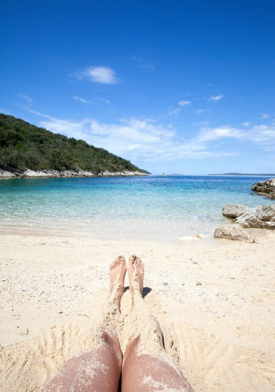 a person laying on a beach with their feet in the sand, by Elizabeth Durack, unsplash, croatian coastline, square, bay, idyllic