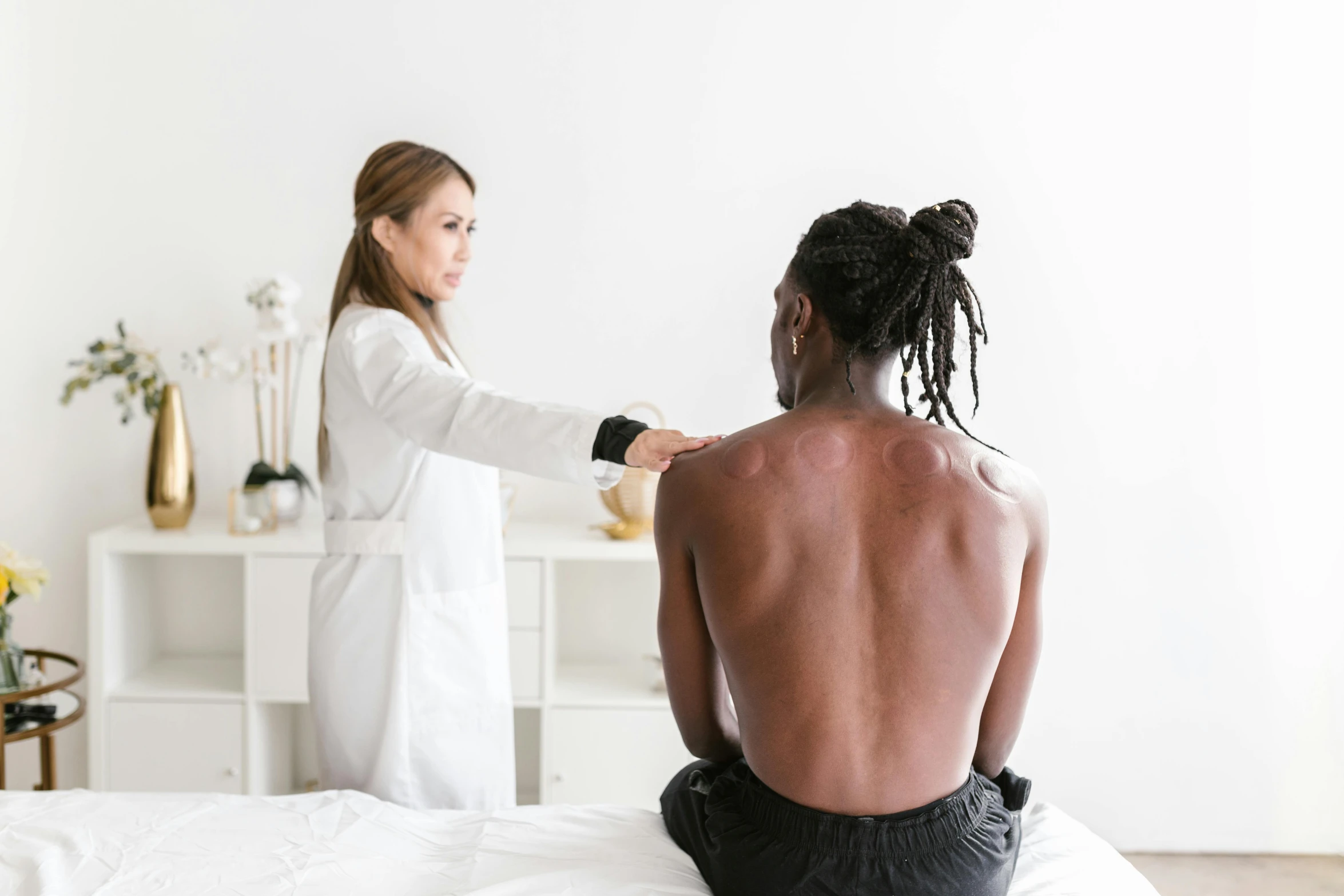 a man sitting on top of a bed next to a woman, pexels contest winner, black human spine, doctors office, showing her shoulder from back, dissection relief