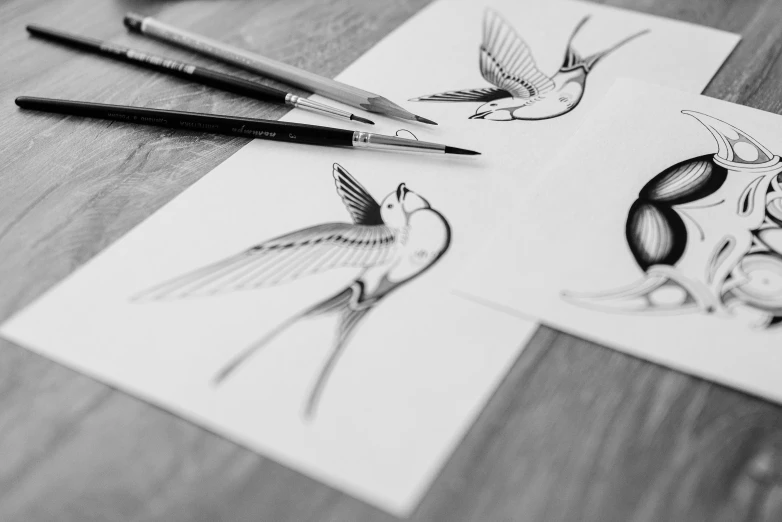 a pair of pencils sitting on top of a piece of paper, an ink drawing, by Mathias Kollros, trending on pexels, bird tattoo, product design shot, flying birds, wood engraving