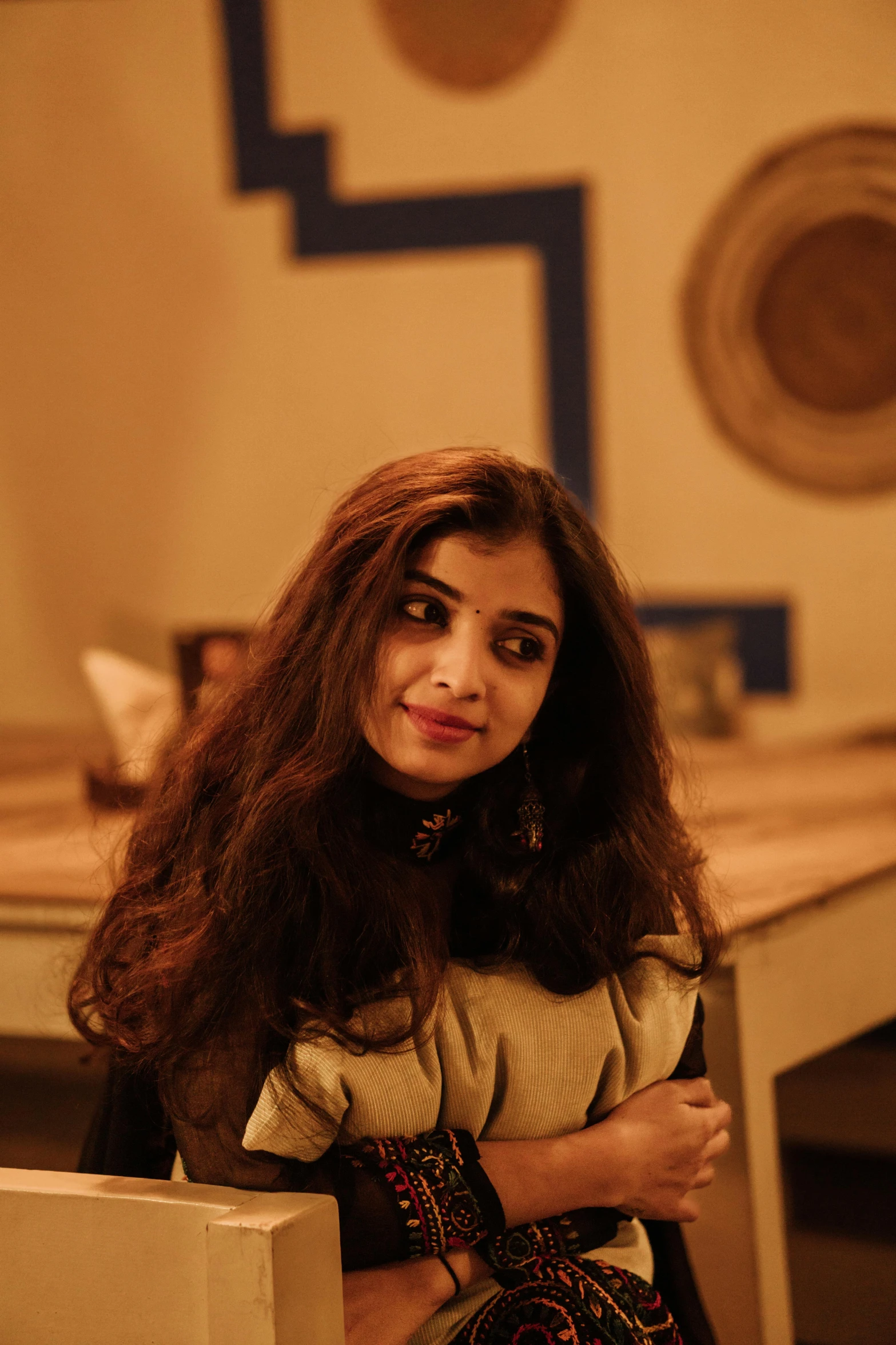 a woman sitting at a table with her arms crossed, inspired by Lubna Agha, pexels contest winner, wavy hair spread out, portrait of ((mischievous)), at college, indiecraft aesthetic