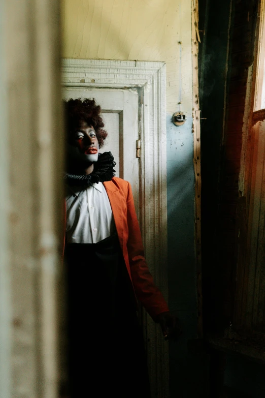 a woman dressed as a clown standing in a doorway, an album cover, inspired by Gordon Parks, unsplash, black and orange, ignant, a handsome, haunted house interior