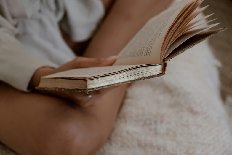 a close up of a person holding an open book, by Carey Morris, trending on pexels, reclining on bed, natural muted tones, storybook, realistic shot