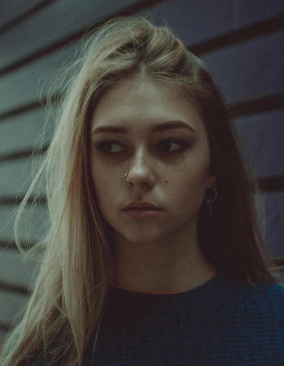 a woman standing in front of a wooden wall, inspired by Elsa Bleda, trending on pexels, realism, portrait of depressed teen, dark blonde hair, piercing stare, desaturated color