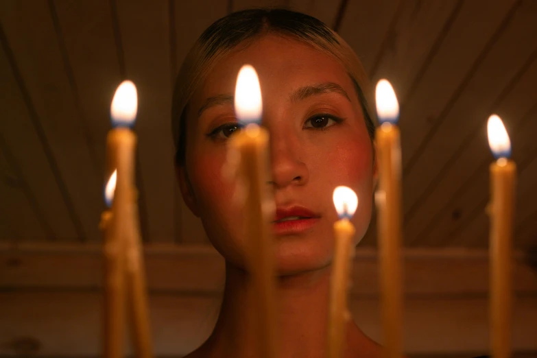 a woman standing in front of a bunch of candles, an album cover, inspired by Elsa Bleda, trending on pexels, hyperrealism, gemma chan girl portrait, holy ceremony, close-up portrait film still, hammershøi