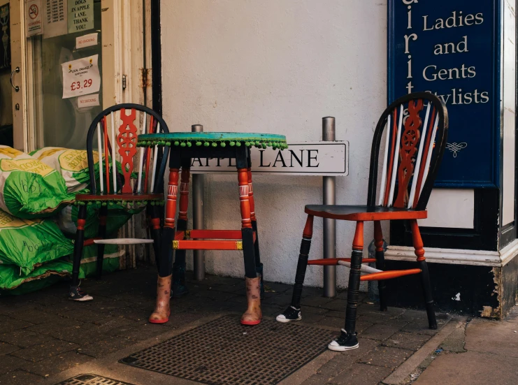 two chairs and a table in front of a store, a photo, pexels contest winner, naive art, red green, long legs, in london, lane brown