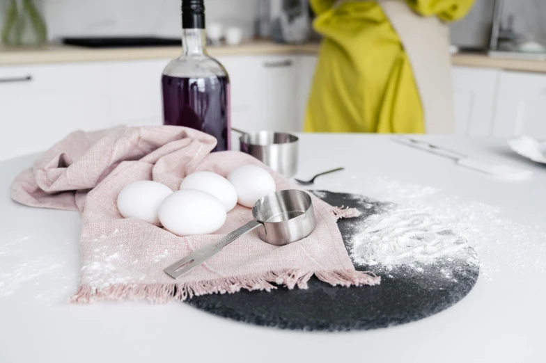 a woman standing in a kitchen next to a counter, a still life, trending on pexels, covered in white flour, magenta and gray, velvet tablecloth, metal kitchen utensils