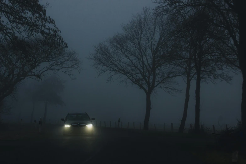 a car driving down a foggy road at night, inspired by Elsa Bleda, pexels contest winner, romanticism, foggy dark graveyard, headlights, ((mist)), light grey mist