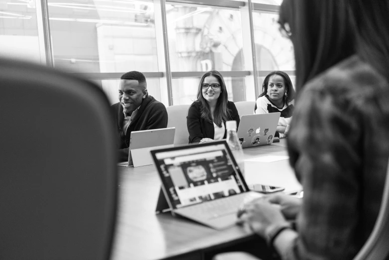 a group of people sitting around a table with laptops, a black and white photo, pexels, teaching, profile picture, diverse, at behance