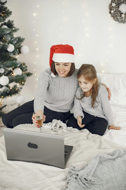a woman and a little girl sitting on a bed with a laptop, wearing festive clothing, grey, promo image, virtual