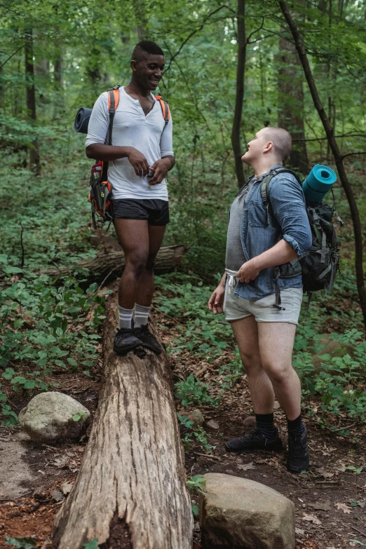 two people standing on a log in the woods, no pants, black man, justin gerard and greg rutkowski, white shorts and hiking boots