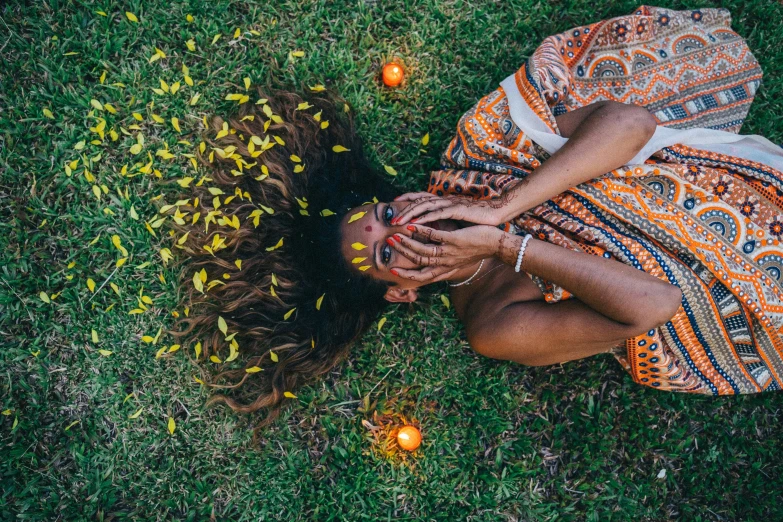 a woman laying in the grass surrounded by oranges, pexels contest winner, afrofuturism, flowers on hair, hippie, taking from above, patterned clothing