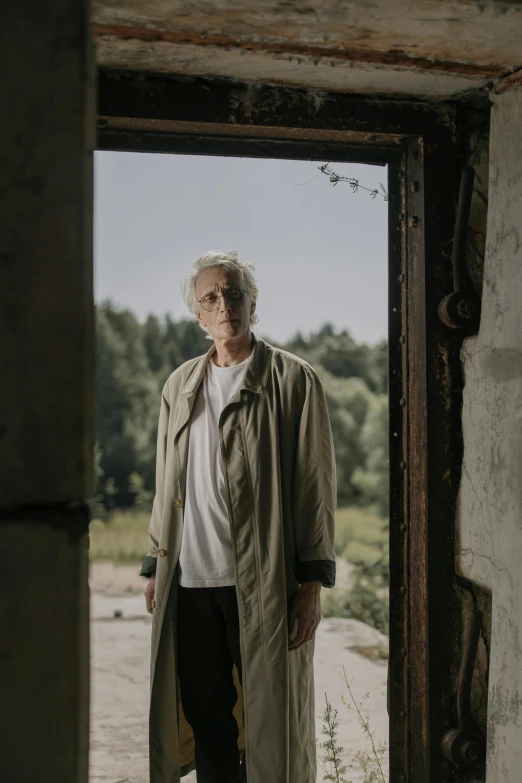 a man in a trench coat standing in a doorway, a portrait, unsplash, magical realism, silver haired, tarkovsky scene, ruins, summer day