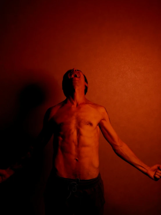 a man standing in front of a red wall, inspired by Bruce Nauman, pexels contest winner, figuration libre, shirtless, dramatic lowkey studio lighting, screaming trent reznor, the suns light is consumed