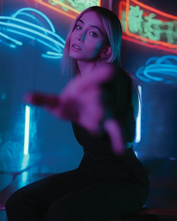 a woman sitting on a stool in front of neon signs, inspired by Elsa Bleda, trending on pexels, frantic dancing pose, ava max, pointing at the camera, moody hazy lighting