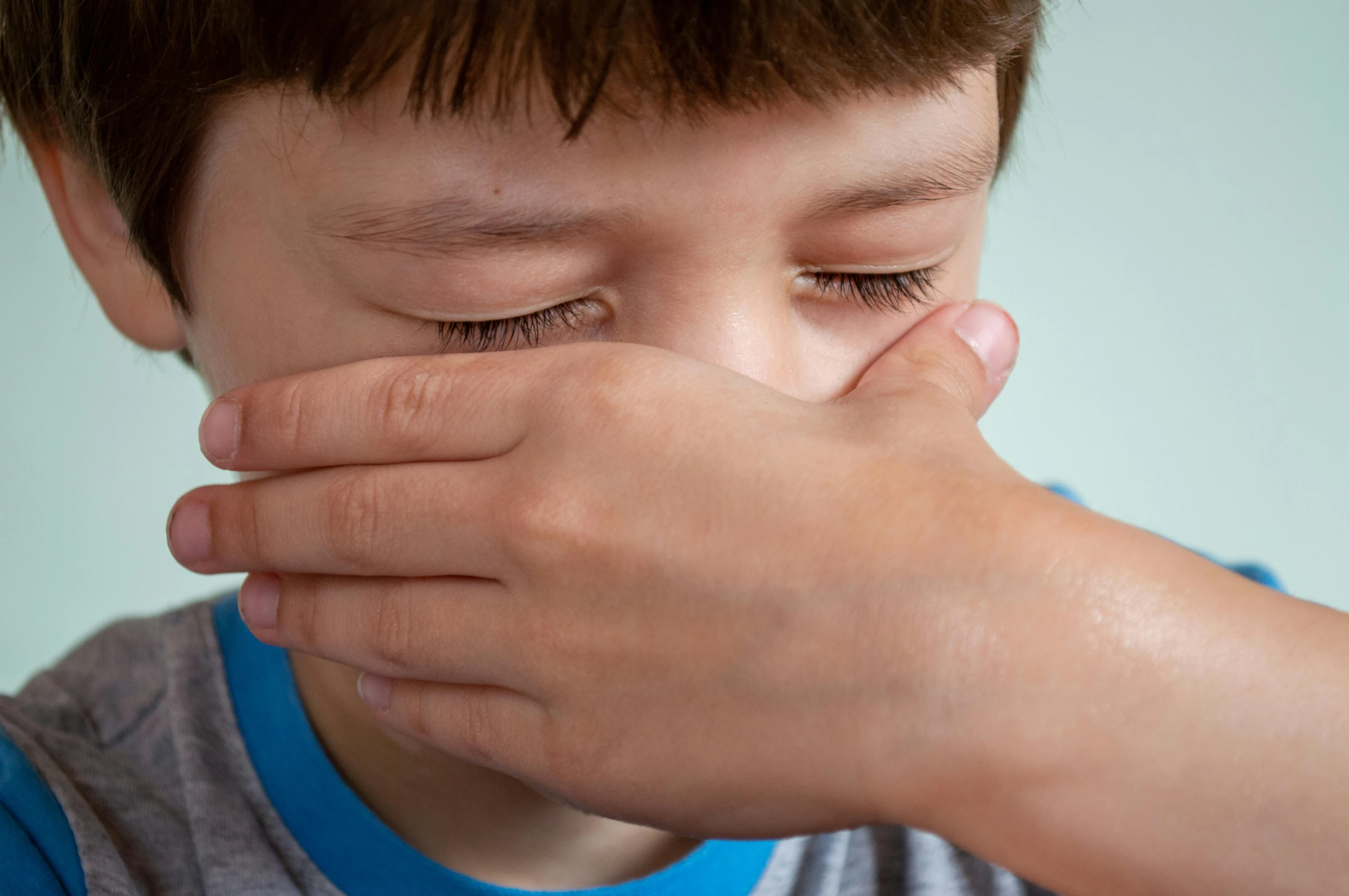 a young boy covers his eyes with his hands, a picture, by Ruth Simpson, shutterstock, visual art, spitting cushions from his mouth, close up shot from the side, nasal strip, hugging his knees