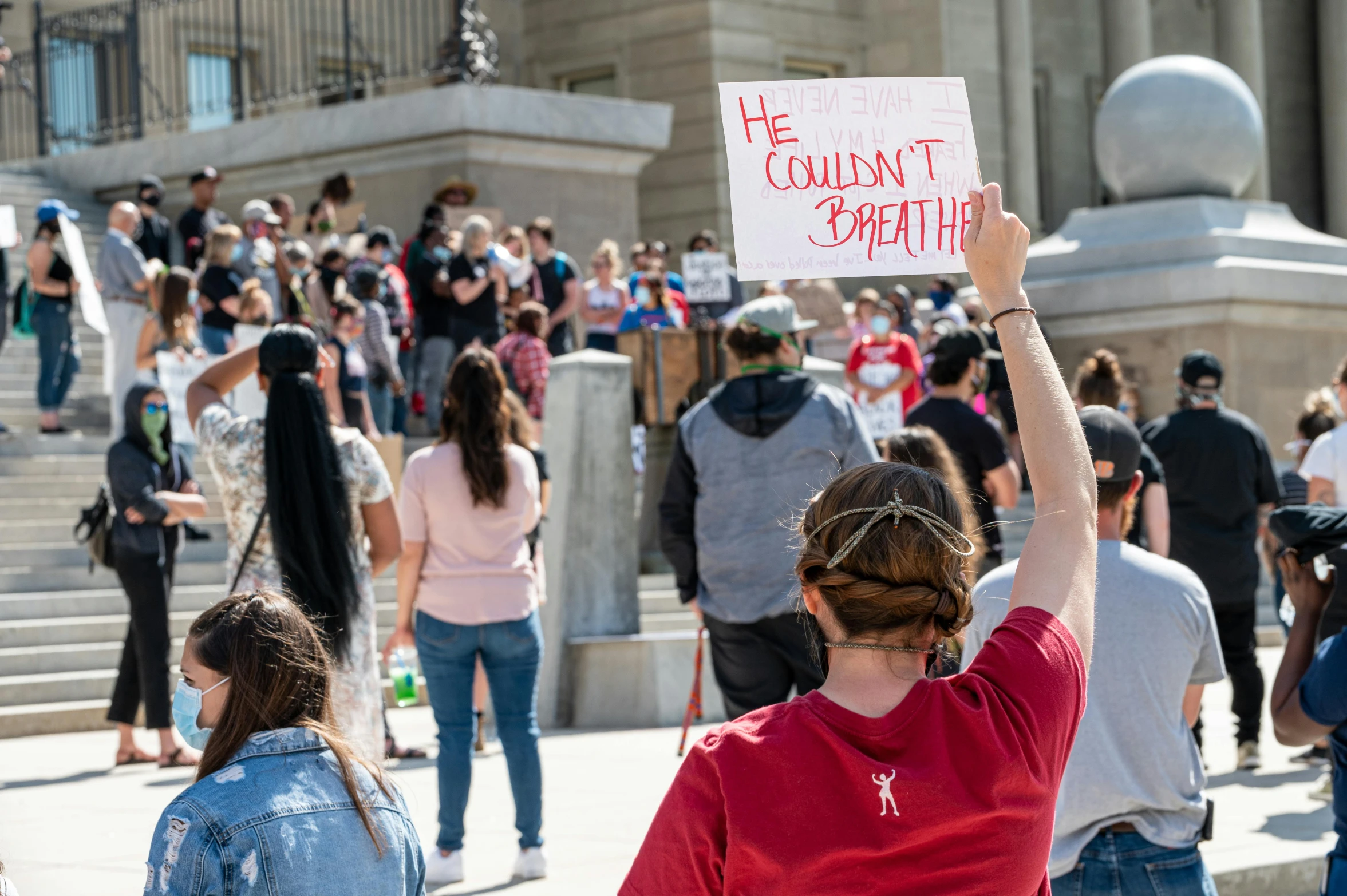 a woman holding a sign in front of a crowd of people, a photo, pexels, sots art, on a marble pedestal, thumbnail, heat wave, tear gas