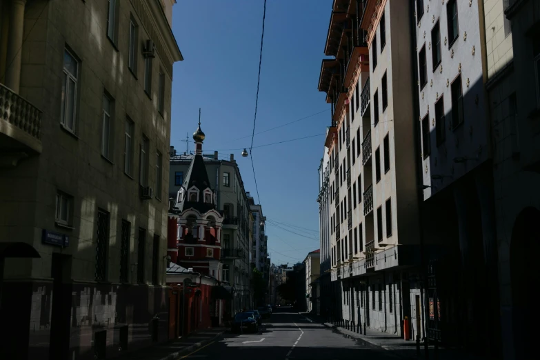 a city street lined with tall buildings and a clock tower, by Andrei Kolkoutine, unsplash, russian temple, shady alleys, low quality photo, pavel shvedov