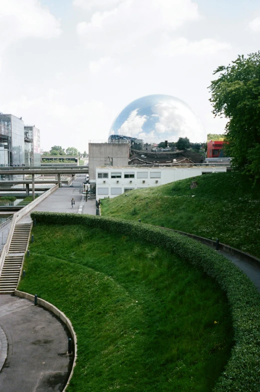 a man riding a skateboard on top of a lush green hillside, paris school, glass sphere, canal, in 2 0 0 2, metallic architecture