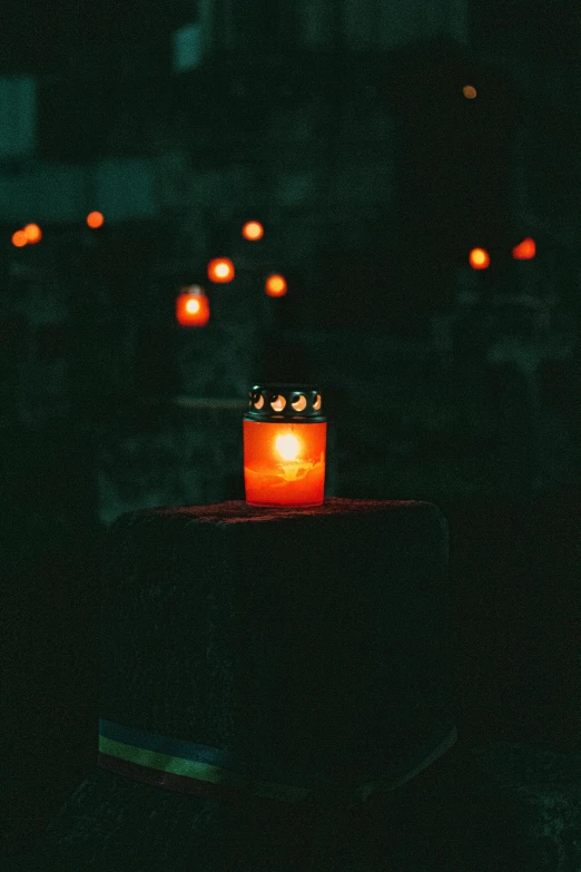 a lit candle sitting on top of a wooden table, in the middle of a graveyard, orange lights, instagram picture, promo image