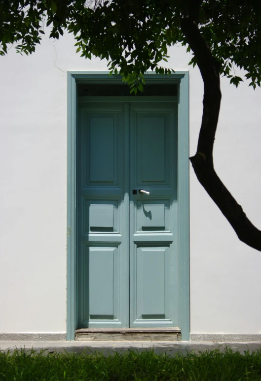 a white building with a blue door and a tree, ((greenish blue tones)), square, azores, marbella