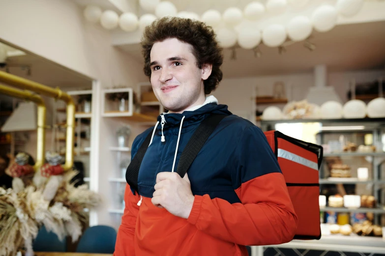 a man with a backpack standing in a store, by Julia Pishtar, arbeitsrat für kunst, timothee chalamet, overweight!! teenage boy, smiling at camera, mechanic