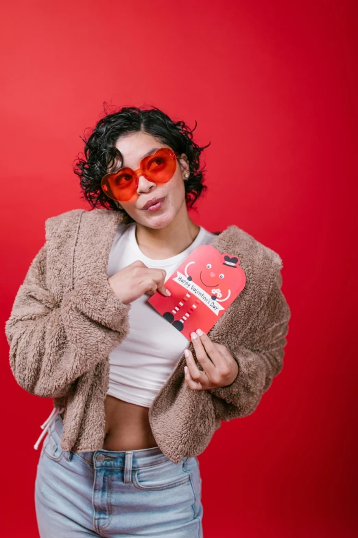 a woman in a jacket and sunglasses holding a book, an album cover, by Julia Pishtar, pexels contest winner, pop art, red flags holiday, full heart - shaped face, non binary model, wearing a red outfit