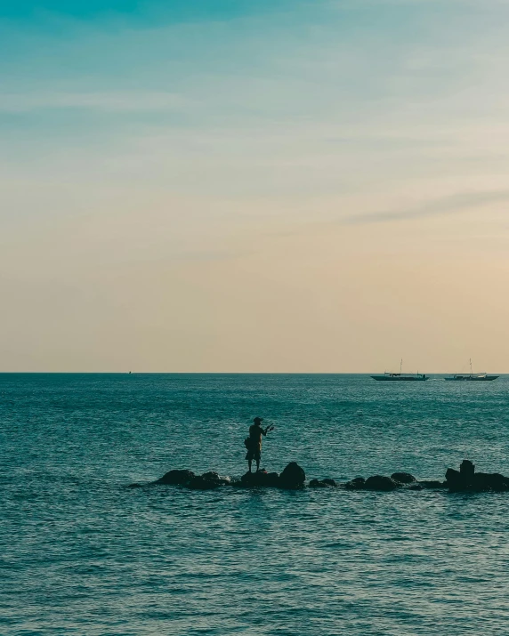 a person standing on a rock in the middle of the ocean, in the distance, lgbtq, set photo, trending photo