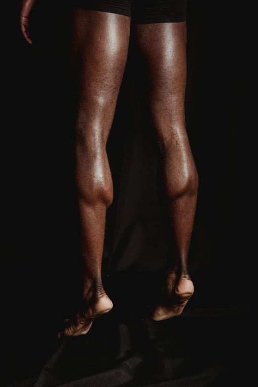 a man standing in front of a black background, by Robert Mapplethorpe, hyperrealism, close-up on legs, adut akech, light-brown skin, skin texture details