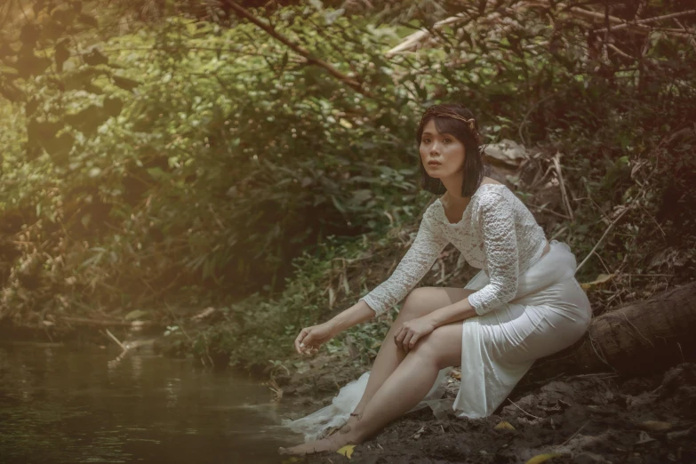 a woman in a white dress sitting next to a body of water, an album cover, inspired by Fernando Amorsolo, pexels contest winner, sumatraism, woman in a dark forest, white sleeves, medium format. soft light, concert