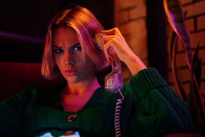 a woman sitting on a couch talking on a phone, a portrait, inspired by Elsa Bleda, trending on pexels, realism, neon operator margot robbie, beaten tech. neo noir style, wearing a green sweater, samara weaving vampire