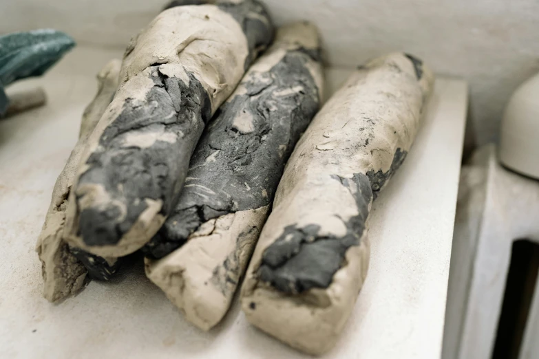 a bunch of bread sticks sitting on top of a counter, by Helen Stevenson, mingei, rotting black clay skin, thick pigmented smoke, covered in bandages, marbled