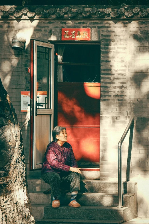 a woman sitting on the steps of a building, by Li Zai, philosopher alvin plantinga, leaning on door, golden hour in beijing, sitting under a tree