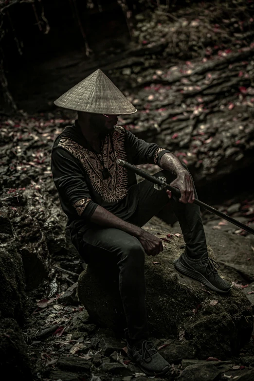 a man sitting on a rock with a hat on, an album cover, inspired by Kanō Hōgai, pexels contest winner, afrofuturism, in a dark space mercenary outfit, vietnam, samurai portrait photo, film still promotional image