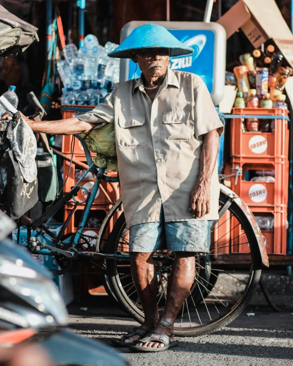 a man that is standing next to a bike, pexels contest winner, sumatraism, markets, wears shorts, thumbnail, wearing wide sunhat