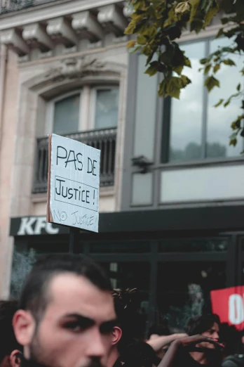a man holding a sign in front of a building, by Raphaël Collin, pexels, justice, parade, instagram picture, kfc