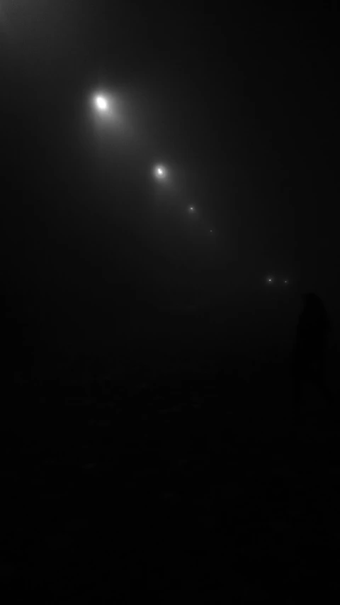 a black and white photo of people walking in the fog, a black and white photo, by Constantine Andreou, conceptual art, lights in the night, scp-049, with black suns in the sky, 'lone dark figure'!!