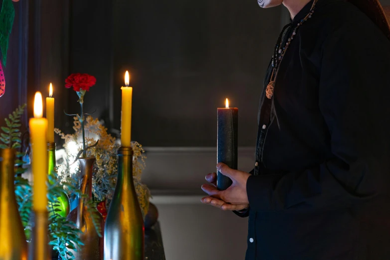 a man standing in front of a table with candles, inspired by Itō Jakuchū, unsplash, vanitas, wearing gothic accessories, holding a candle, close up shot from the side, priest