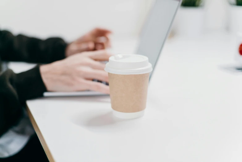 a person sitting at a table with a laptop and a cup of coffee, by Nicolette Macnamara, paper cup, professional product shot, zoomed in, small