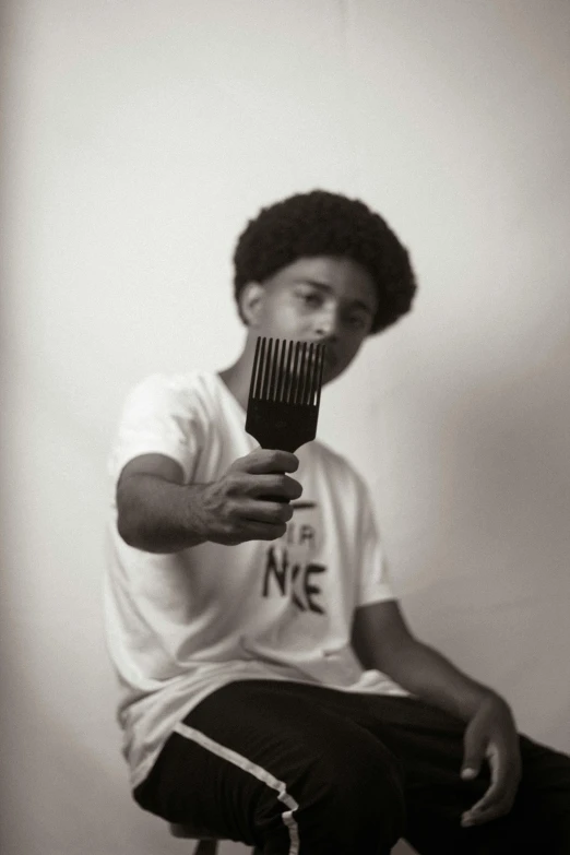 a man sitting on a stool holding a comb in his hand, by Afewerk Tekle, pexels contest winner, black arts movement, boy hair, headshot profile picture, curl noise, tommy 1 6 years old
